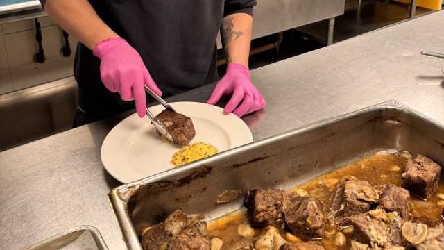 man in commercial kitchen with a metal tray of meat