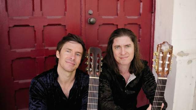 Roman Street- Two men in front of red door sitting with guitars