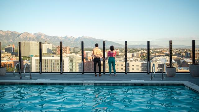 View of downtown Salt Lake looking across a pool with 2 people standing near the edge overlooking the city