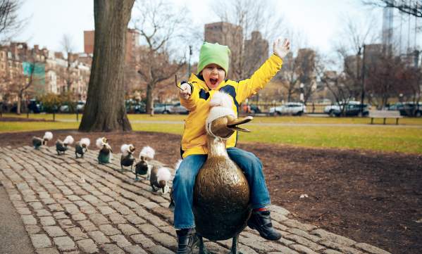 Child sitting on duck statue with line of duckling statues lined up behind it