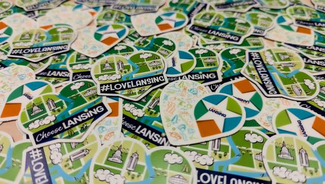 collection of Choose Lansing heart-shaped stickers spread across a table, showcasing the brand's vibrant and local flair.