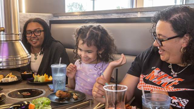 Family enjoying a shared meal at KPOT Korean BBQ & Hot Pot, cooking food together at the table.