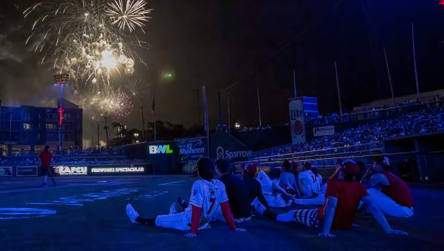 People sitting on the  baseball field watching the fireworks over Jackson Field