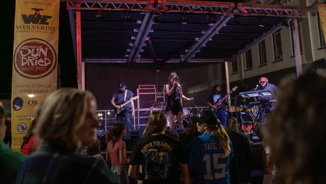 A band performing on a stage at the Sundried music festival with a crowd watching