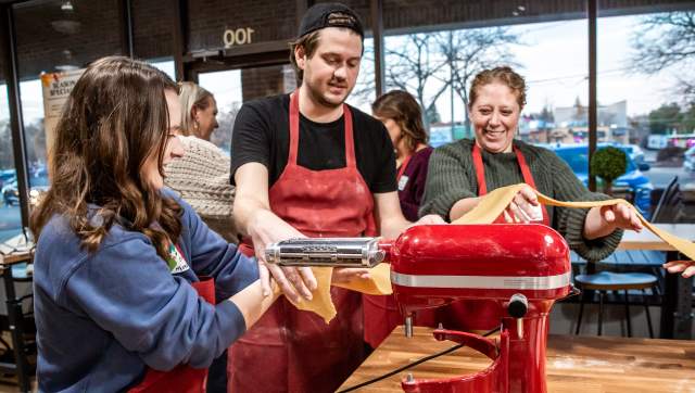 Three people standing around a mixer, making pasta.