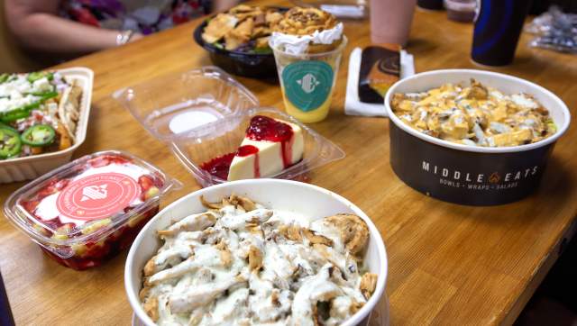 A spread of chicken shawarma bowls, desserts, loaded fries, a salad, and a smoothie sitting on a booth table at Middle Eats.