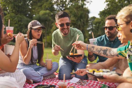 Group of friends enjoying sushi and bubble tea on a picnic blanket in the park