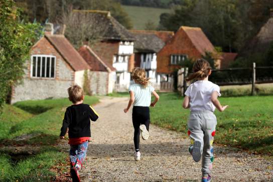 Three children run along the path towards the old buildings at Weald and Downland museum, Sussex
