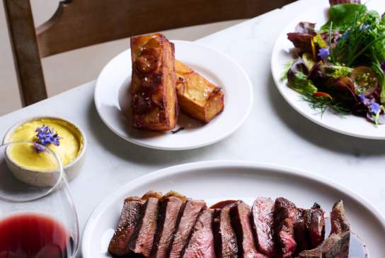 A table set up with plates of roasted meat, sides and a glass of red wine at Knepp Wilding Kitchen