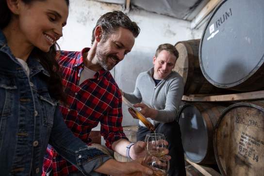 Couple enjoying a tour at Killowen Distillery while the guide pours liquid into their glasses for sampling