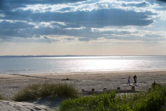 Sunny day at West Wittering beach looking out to sea, with a couple walking in the sandy dunes