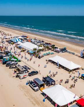 Aerial shot of a long stretch of beach covered in tents and people during a festival.