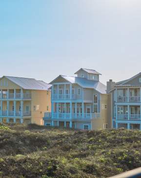 row of 4 large beach houses nestled in dunes in bright sunlight