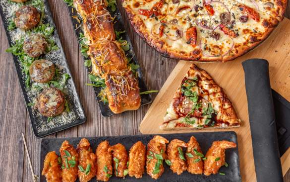 An image of chicken wings, pizza, pizza rolls, and other appetizers spread across a table showcasing the menu at doc & bubbas