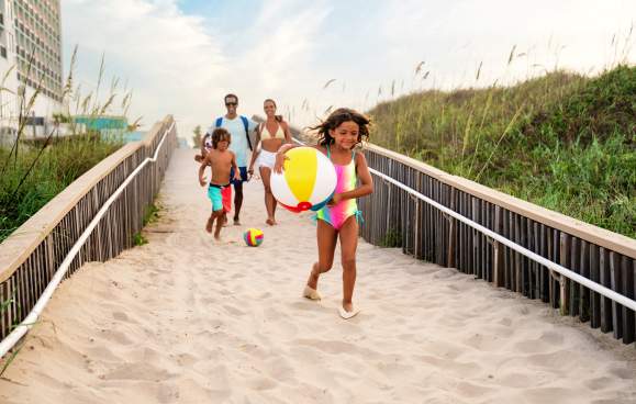 Family Running Down Beach Access Point