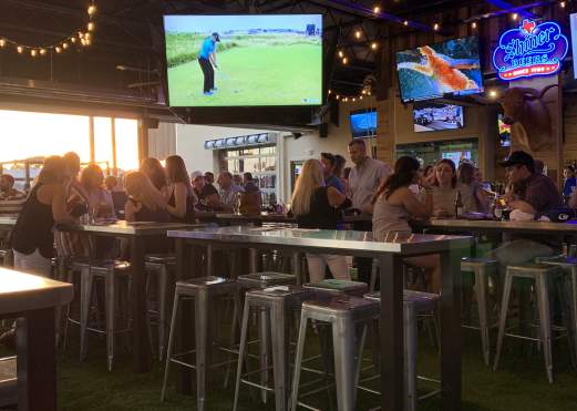 Big screen TV and patrons sitting at high table tops at Little Woodrow's Sports Bar