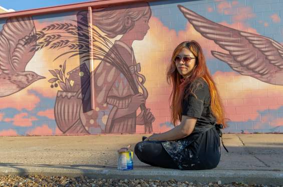 Amy Sol sits in front of her mural