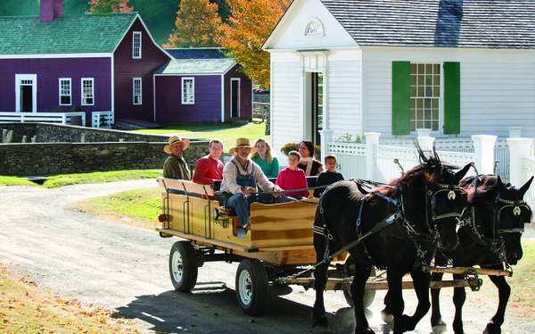 an image of a horse drawn carriage carrying people in front of historic houses with fall leaves behind it