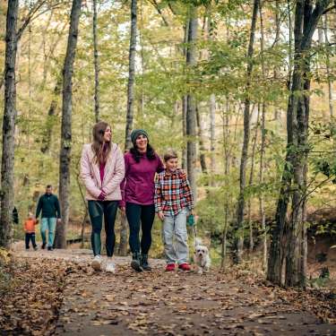family walking on a paved trail through the woods in the fall
