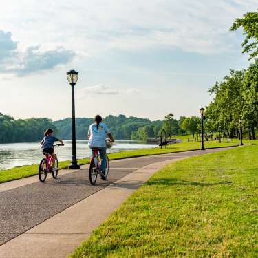 two girls ride bikes along a paved path next to a river