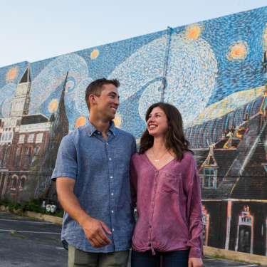 man and woman in front of a large mural