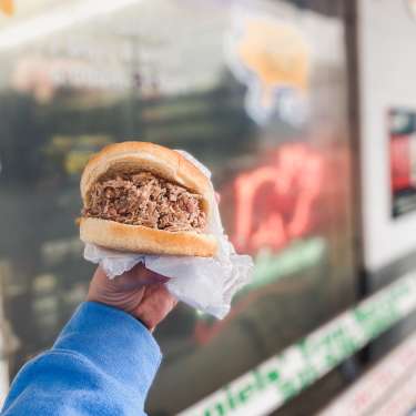 hand holding a large pulled pork sandwich