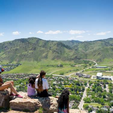 Family on a hike sitting down and looking off North Table Mountain over Golden in the Spring