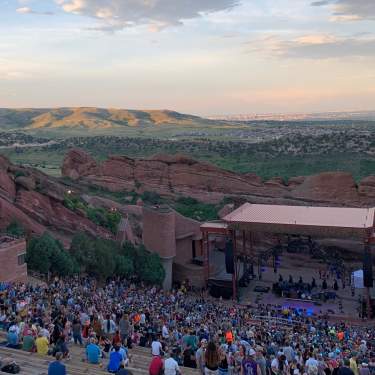 Red Rocks Amphitheatre crowds gathering before a show while it's still light out in the evening with Green Mountain and metro Denver in the background.