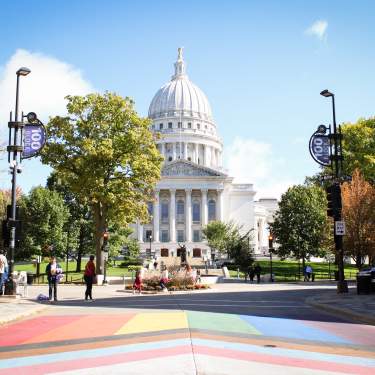 A wide shot of the Wisconsin State Capitol building from State Street with a view of the rainbow pride crosswalk