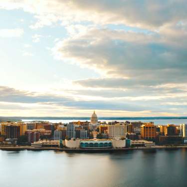 A wide shot downtown Madison surrounded by two lakes, one in the foreground and one in the background. The Wisconsin State Capitol is in the center.