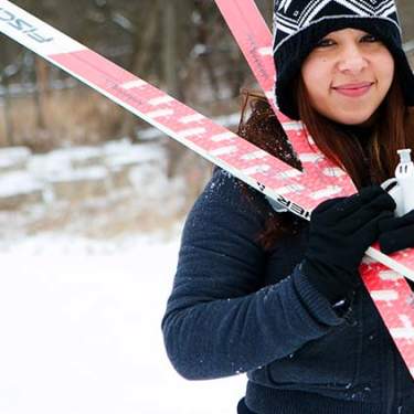 A young woman dressed in snow gear holds her skis over her shoulder in Busse Woods