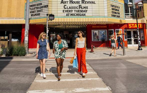 Three women walking across the crosswalk in front of the State Theatre