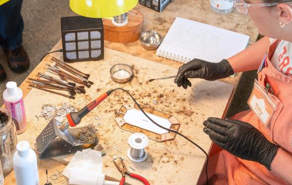 Woman in progress of a workshop demonstration. She's wearing black gloves and holding a crafting utensil in her right hand.