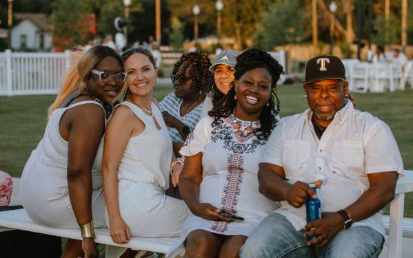 Photo of a group seated at a picnic table at the Brownwood Event Center front lawn for the White Linen Party.