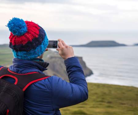 A person in a bobble hat taking a photo of Worm's Head