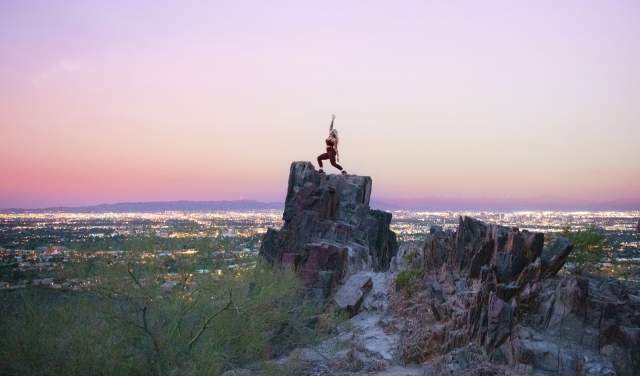 A woman does a yoga pose on top of Piestewa Peak in Phoenix at sunrise