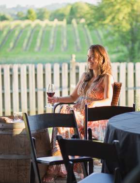 Woman sitting down enjoying a wine tasting at 8 Chains North with the vineyard in the background