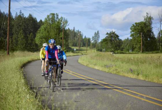 A group of three women cycle on a country rode in the summertime.