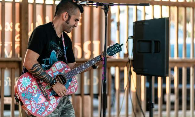 A guitarist rocks out with a red guitar covered in stickers.