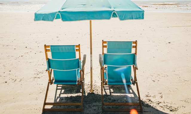 Two blue beach chairs set up on the beach with an unbrella between