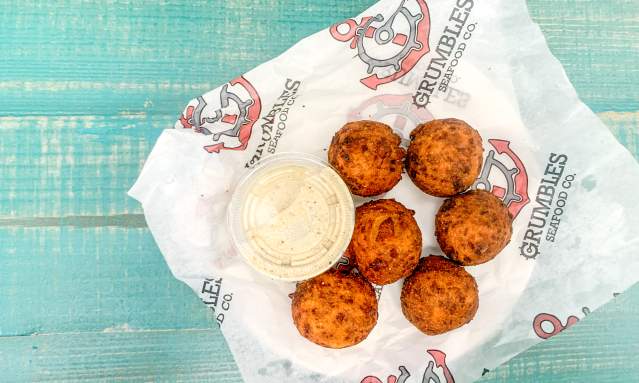 A plate of hushpuppies with a sauce sits on a light teal table
