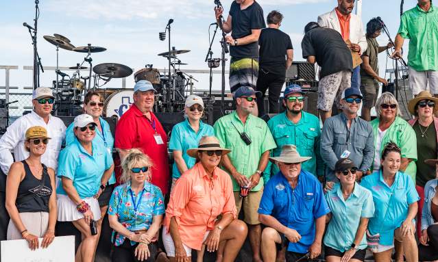 A group of people poses in front of a stage on the beach, smiling at the camera