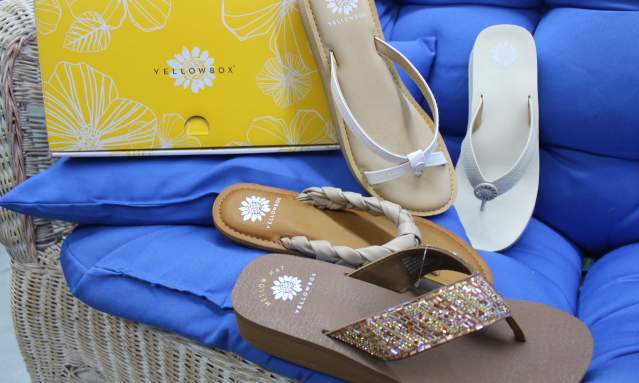 Four flip flops sit on a blue couch next to a yellow shoe box.