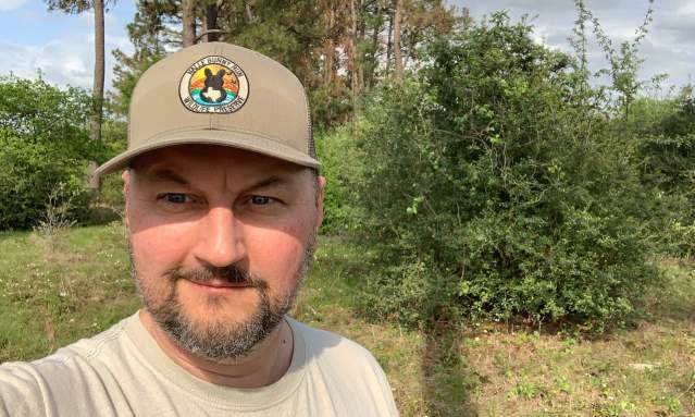 Selfie of a man wearing a hat in front of a natural green setting