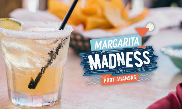 A margarita sitting on a table with chips int he background. To the right of the margarita is a blue and orange logo that says Margarita Madness Port Aransas