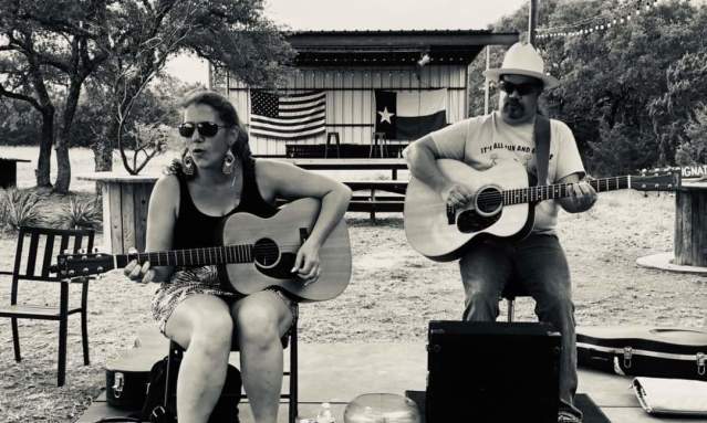 A man and a woman, each with guitars, sit on barstools and perform.