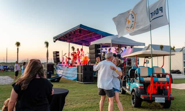 A couple dances in front of a music stage and next to a golf cart with Port Aransas flags