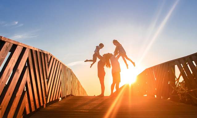 Parents lift their two children in the air on a boardwalk at sunrise in Port Aransas. Texas