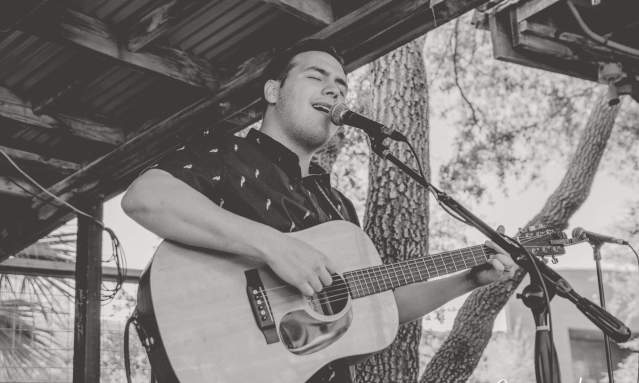 Black and white photo of a man singing into a microphone and strumming a guitar