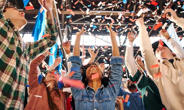 People with their arms up, cheering and confetti falls on them
